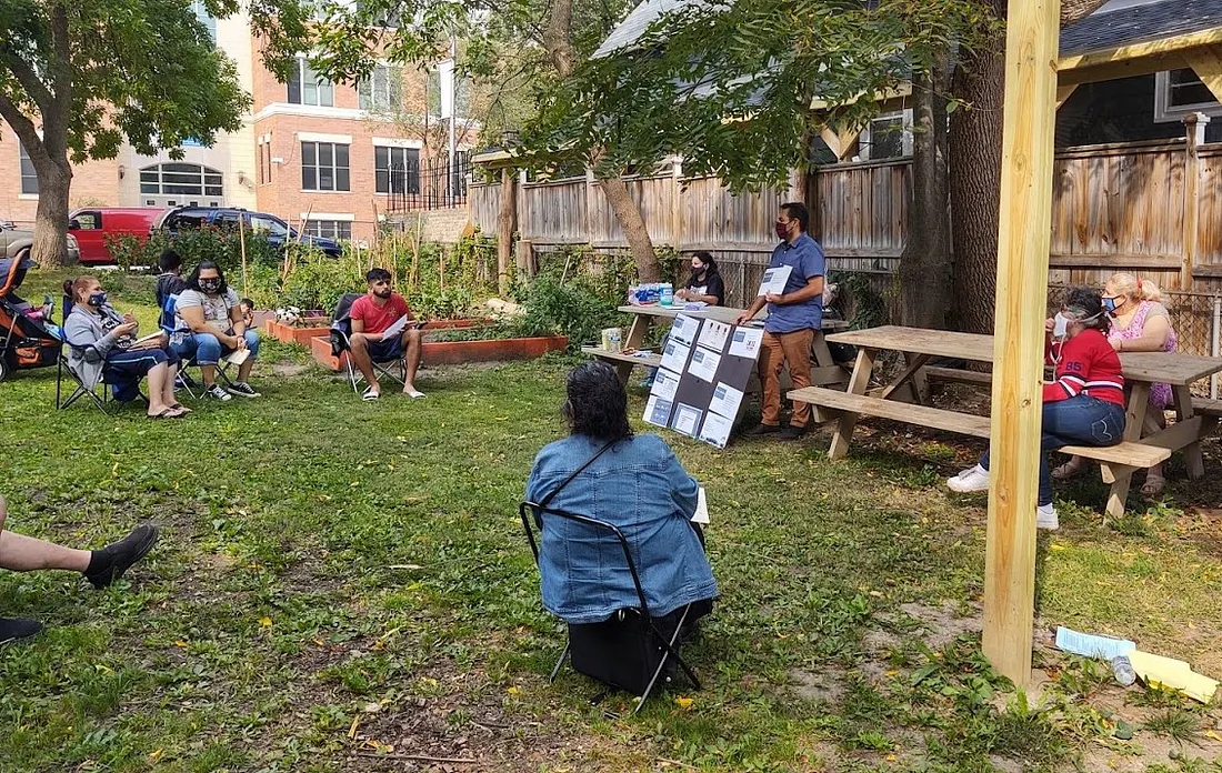 Residents from Milwaukee’s Clark Square neighborhood are sitting in a circle in a meeting outside.